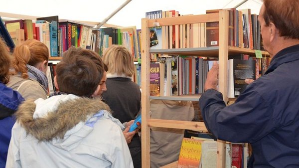 Junge und ältere Besucher:innen laufen zwischen Bücherregalen herum.