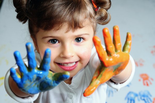 Mädchen mit blauer und oranger Fingermalfarbe an den Händen.