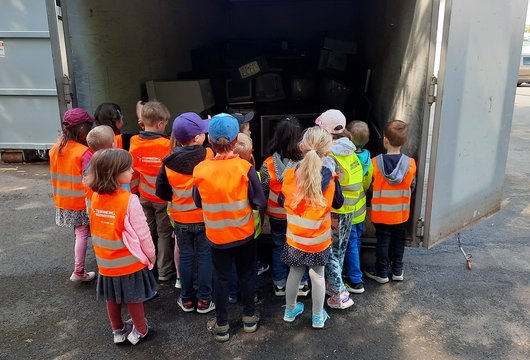 Gruppe von Kindern in Sicherheitswesten schaut in einen Container.