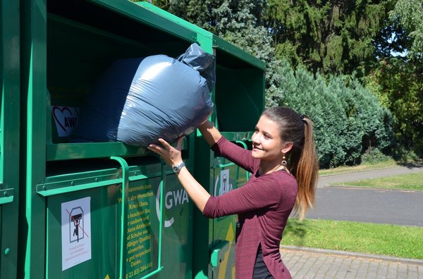 Eine junge Frau wirft einen blauen Sack in einen Altkleidercontainer.